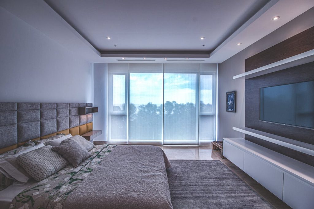 Spacious luxury bedroom with a modern design, featuring a large window and a wall-mounted TV.